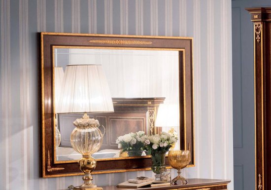 Ορθογώνιος καθρέφτης σχεδιασμένος σε χρώμα καρυδί και διακοσμημένος με χρυσές αγκράφες.