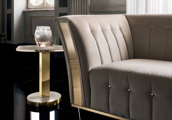 Καναπές σχεδιασμένος σε χρώμα μπεζ με χρυσές λεπτομέρειες και ψηλά μπράτσα.