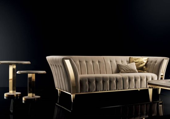 Καναπές ο οποίος είναι σχεδιασμένος σε χρώμα μπεζ και διακοσμημένος με ψηλά μπράτσα και χρυσές λεπτομέρειες.