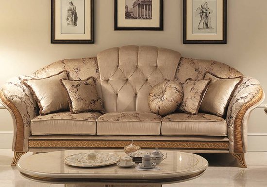 Τριθέσιος μπεζ καναπές ο οποίος είναι διακοσμημένος με χρυσές λεπτομέρειες και λουλούδια.