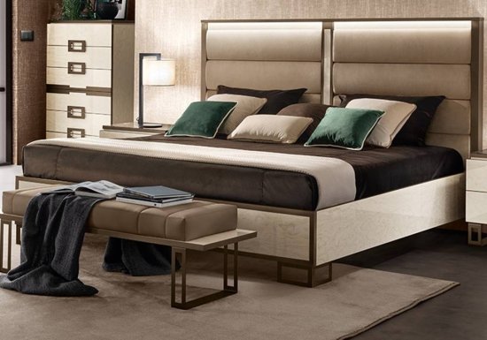 Κρεβάτι το οποίο είναι σχεδιασμένο σε χρώμα εκρού και διακοσμημένο με καφέ μεταλλικές λεπτομέρειες. Διαθέτει κεφαλάρι το οποίο είναι ντυμένο με ύφασμα.